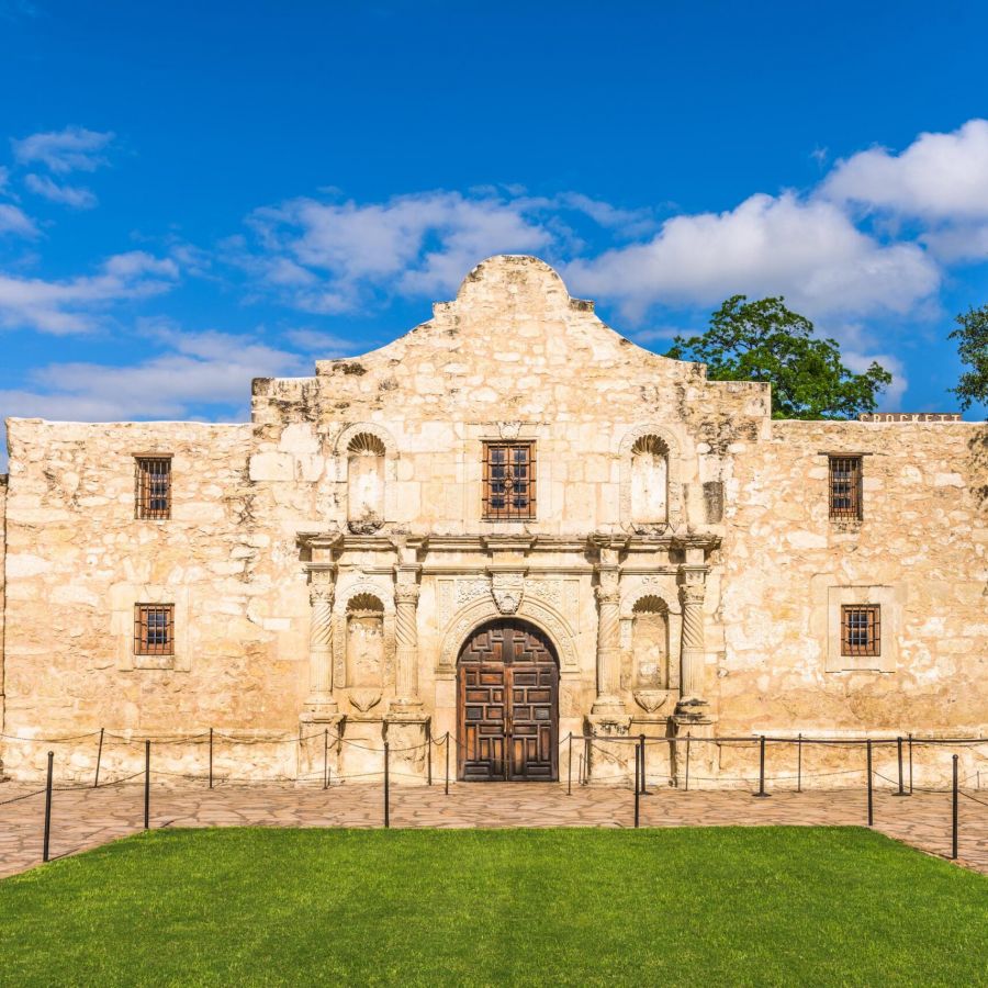 Enclave at the Dominion The historic Alamo building with a Texas flag and lush green lawn under a clear blue sky.